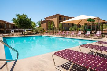 A pool with a white umbrella and red chairs.